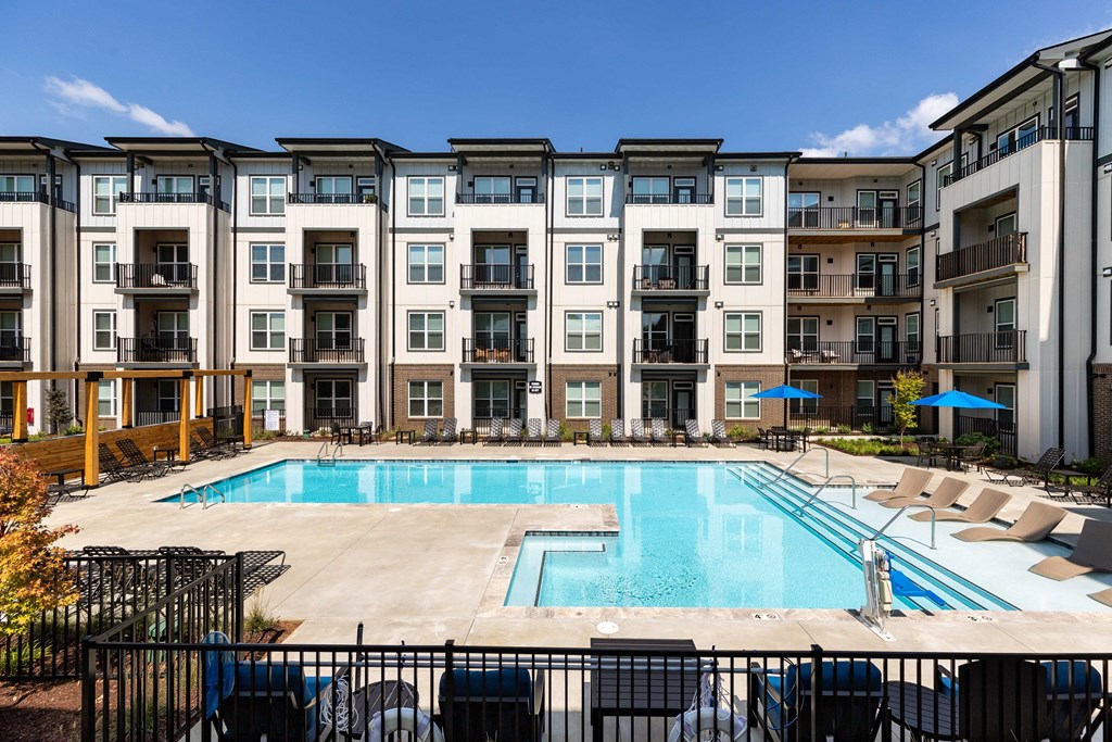 a swimming pool with chairs around it in front of an apartment building at Abberly Liberty Crossing Apartment Homes, North Carolina