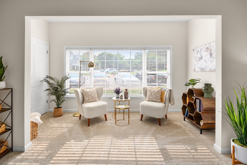 a living room with two white chairs and a table in front of a large window at Abberly Grove Apartment Homes, Raleigh, NC