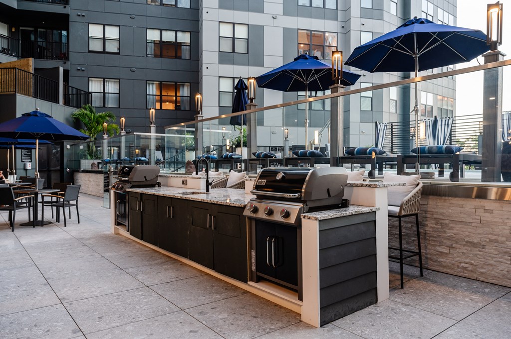 an outdoor patio with a barbecue grill and tables with umbrellas