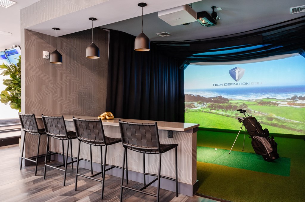 a room with a golf simulator and a bar with a guitar