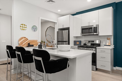 A kitchen with white cabinets and black chairs.