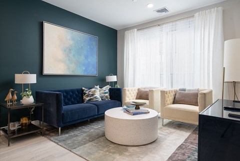 A living room with a blue couch, a white coffee table, and a painting on the wall.
