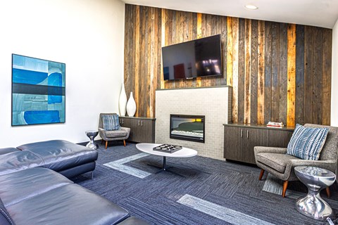 A modern living room with a grey sofa, a grey armchair, a white coffee table, a TV on the wall, and a wooden wall paneling.
