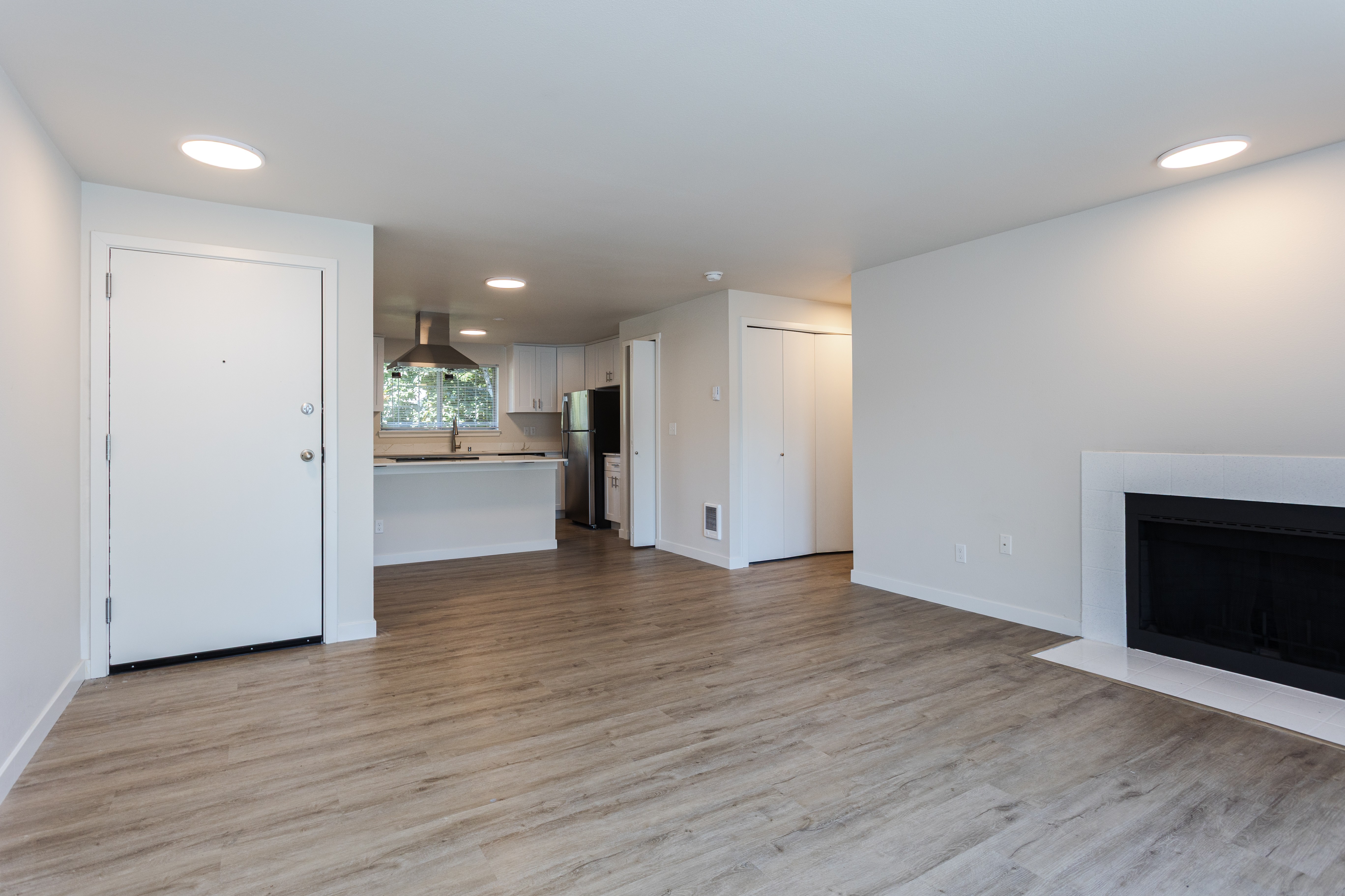 A white interior with a fireplace and a kitchen in the background.