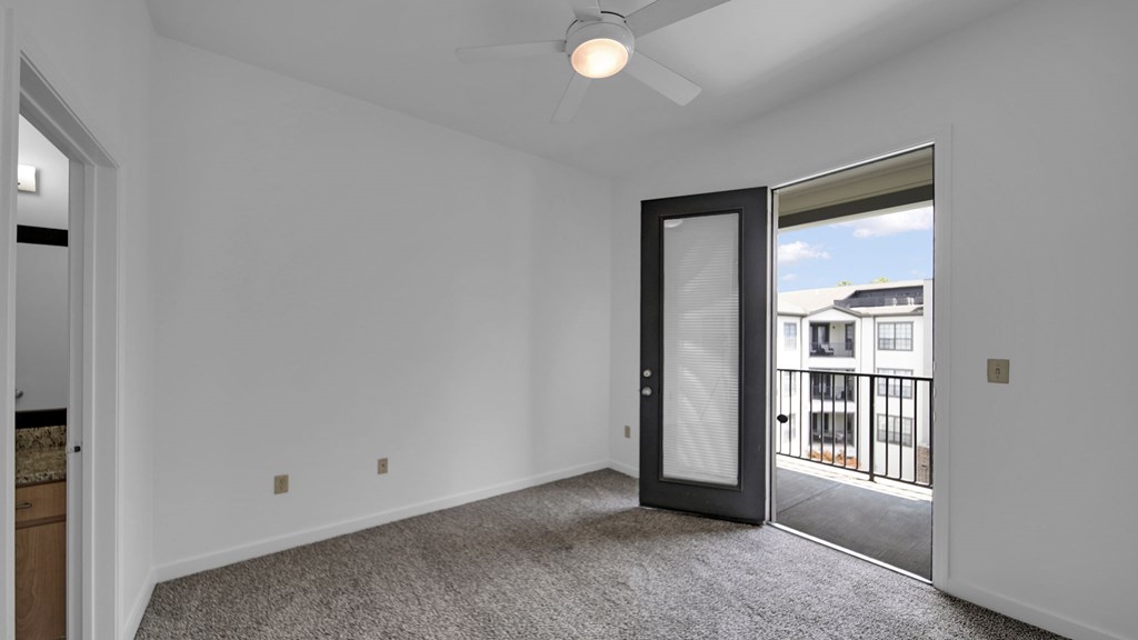 A room with a ceiling fan and a door leading to a balcony.