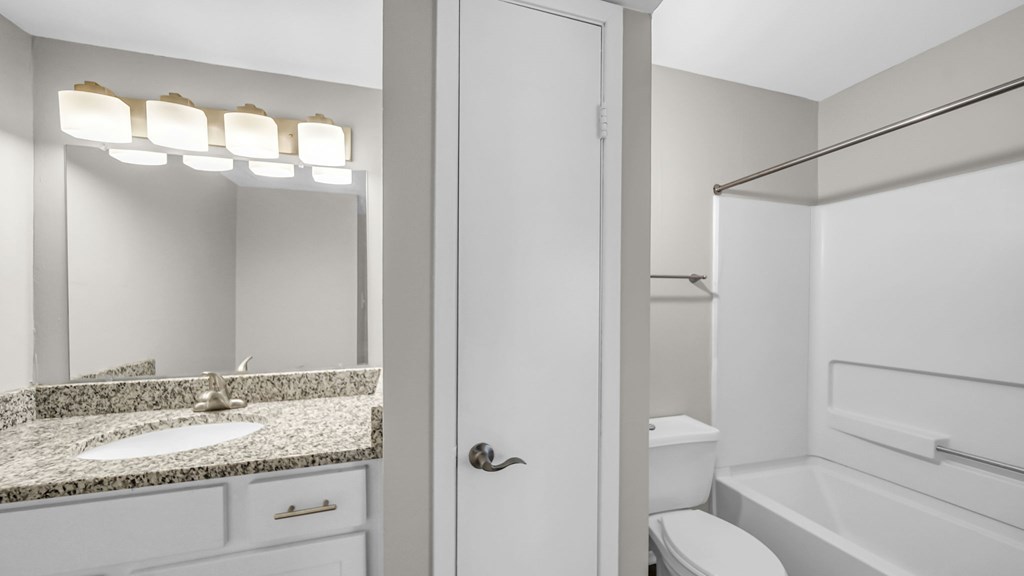 A white bathroom with a sink, mirror, and toilet.