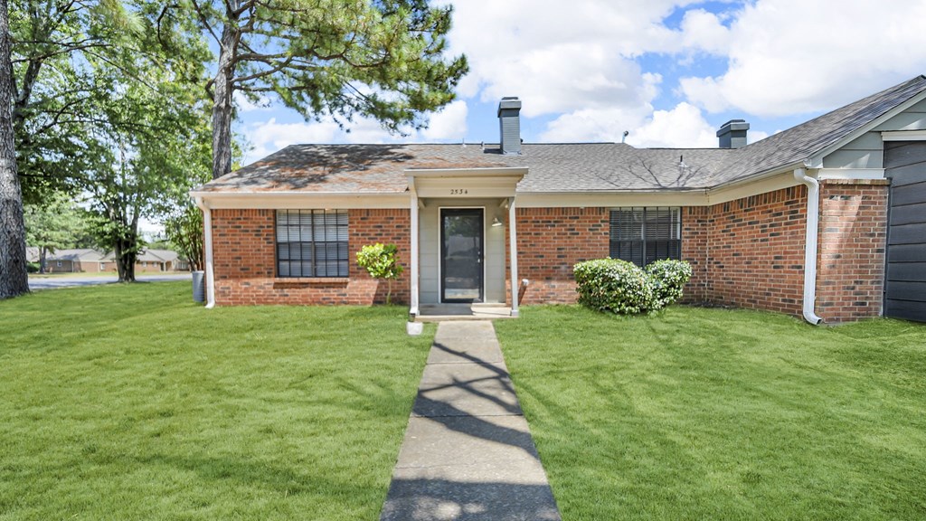 A red brick house with a green lawn in front.