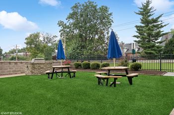 two picnic tables on the grass in front of a patio with umbrellas at CWE Apartments, St. Louis, MO
