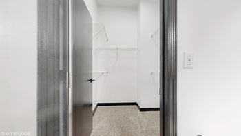 a walk in closet in a white room with a silver door