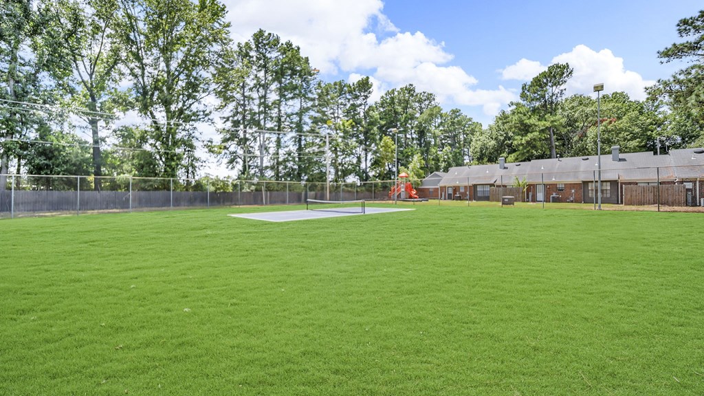 A large grassy field with trees in the background and a building to the right.