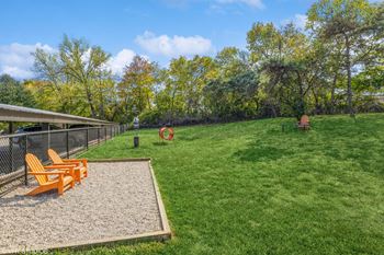 a fenced in dog park with a gravel area and orange chairs at Runaway Bay Apartments, Columbus, OH
