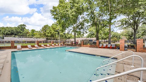 A large outdoor swimming pool surrounded by trees and lounge chairs.
