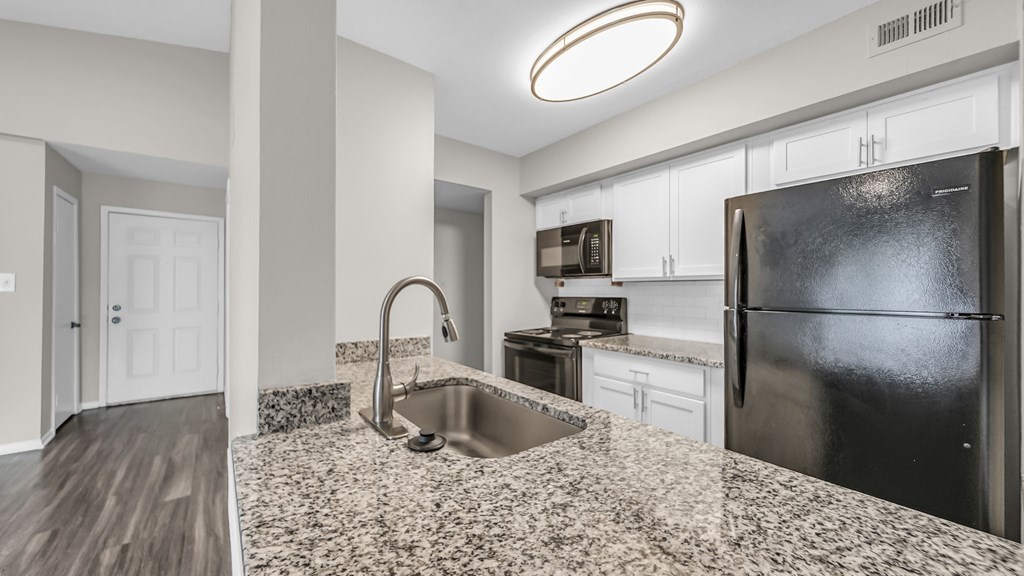 A kitchen with a black refrigerator and a sink with a granite countertop.