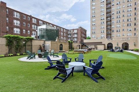 A lawn with chairs and tables is surrounded by buildings.