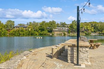 a picnic table on a stone patio overlooking a lake at Runaway Bay Apartments, Columbus