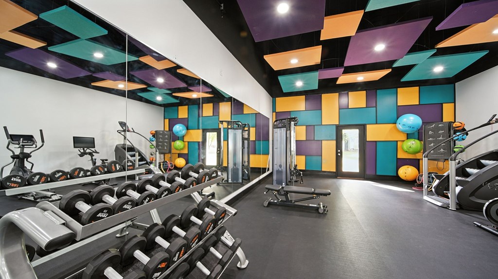 A gym with a variety of equipment including dumbbells, weight machines, and exercise balls.