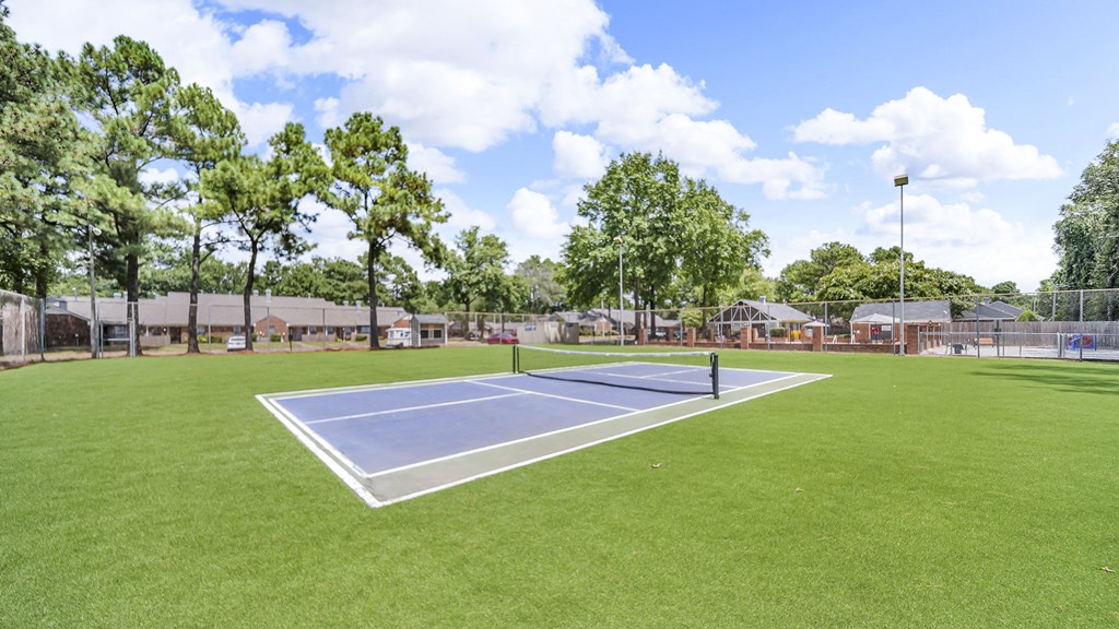 A tennis court surrounded by trees and a fence.