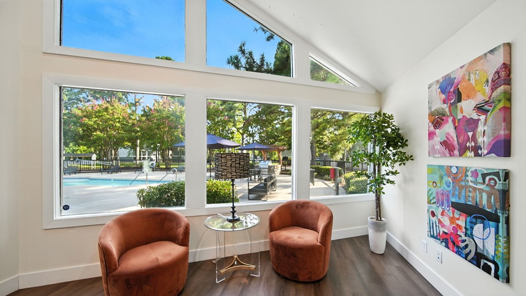 Two brown chairs are placed in front of a wall with a painting and a potted plant.