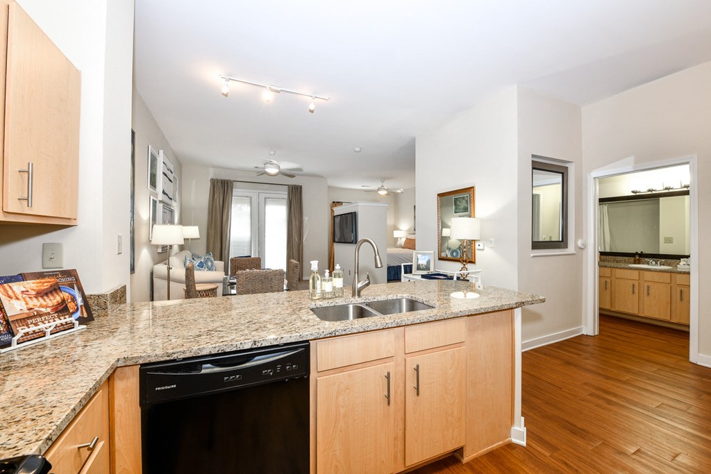 a kitchen with granite countertops and wooden cabinets with a living room in the background
