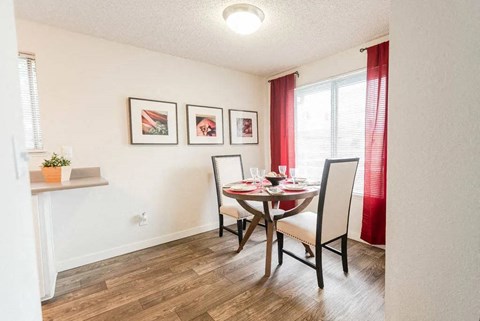 A dining room with a table set for two and a potted plant on the windowsill.