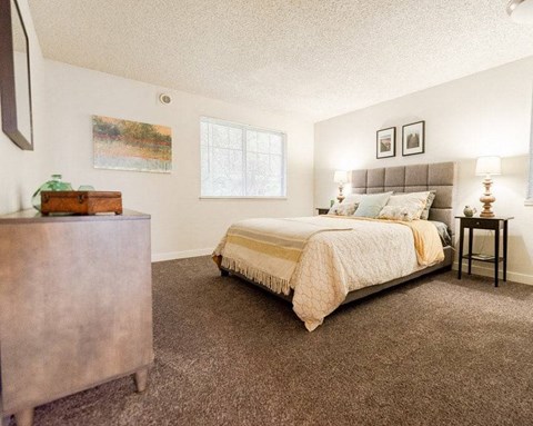 A bedroom with a bed, nightstand, and a painting on the wall.