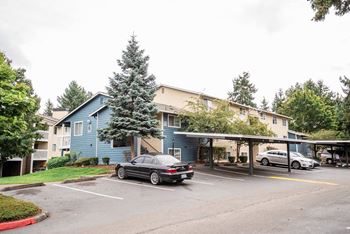 A parking lot with cars and a blue building in the background at Altitude Apartment , Tacoma, Washington