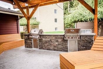 A wooden deck with a stone wall and a grill is in the foreground at Altitude Apartment , Tacoma, 98444