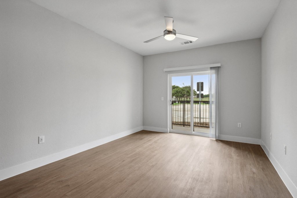 an empty living room with wood flooring and a sliding glass door to a balcony at The Virginia, Seguin, 78155