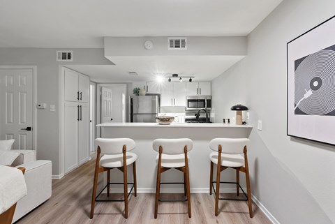 A kitchen with white cabinets and a white fridge with a bar area in front.