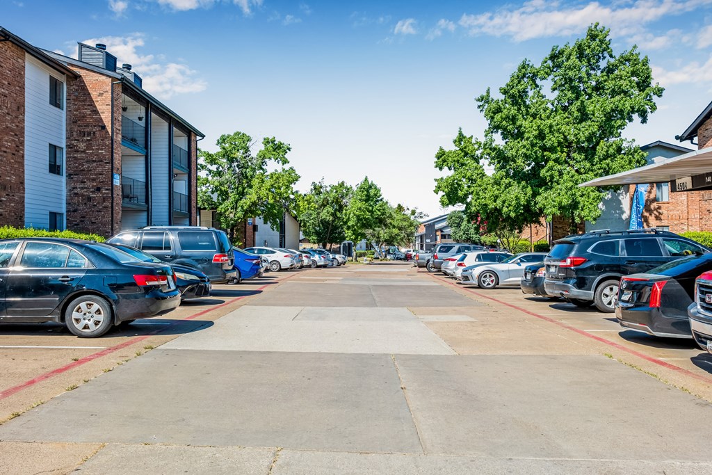 A parking lot with cars parked in rows and apartment buildings in the background.