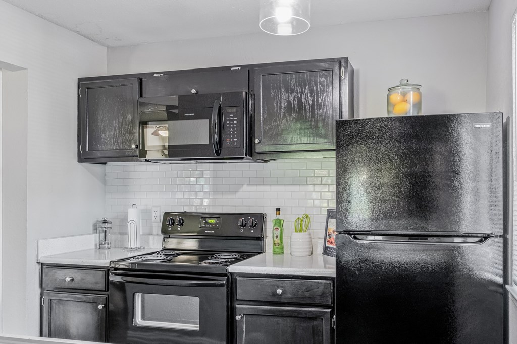 A black fridge stands in a kitchen with black appliances and white countertops.