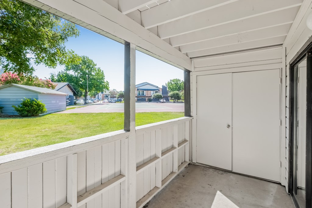 A white wooden balcony with a white door and a window overlooking a green lawn and a blue house.