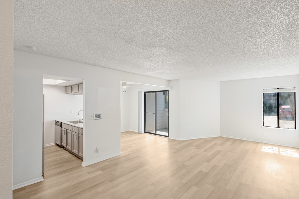 A sparsely furnished room with a kitchen area in the background.