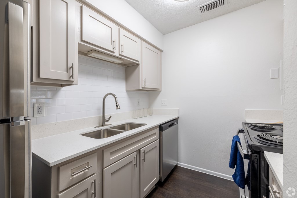 A kitchen with a stainless steel refrigerator, a white sink, and a white countertop at Sunset Canyon Apartments, Texas
