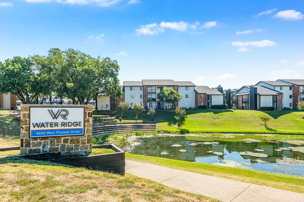 A sign for Water Ridge sits in front of a pond and houses.