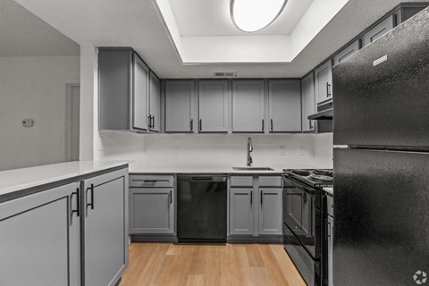 A black refrigerator is on the right in a kitchen with grey cabinets.