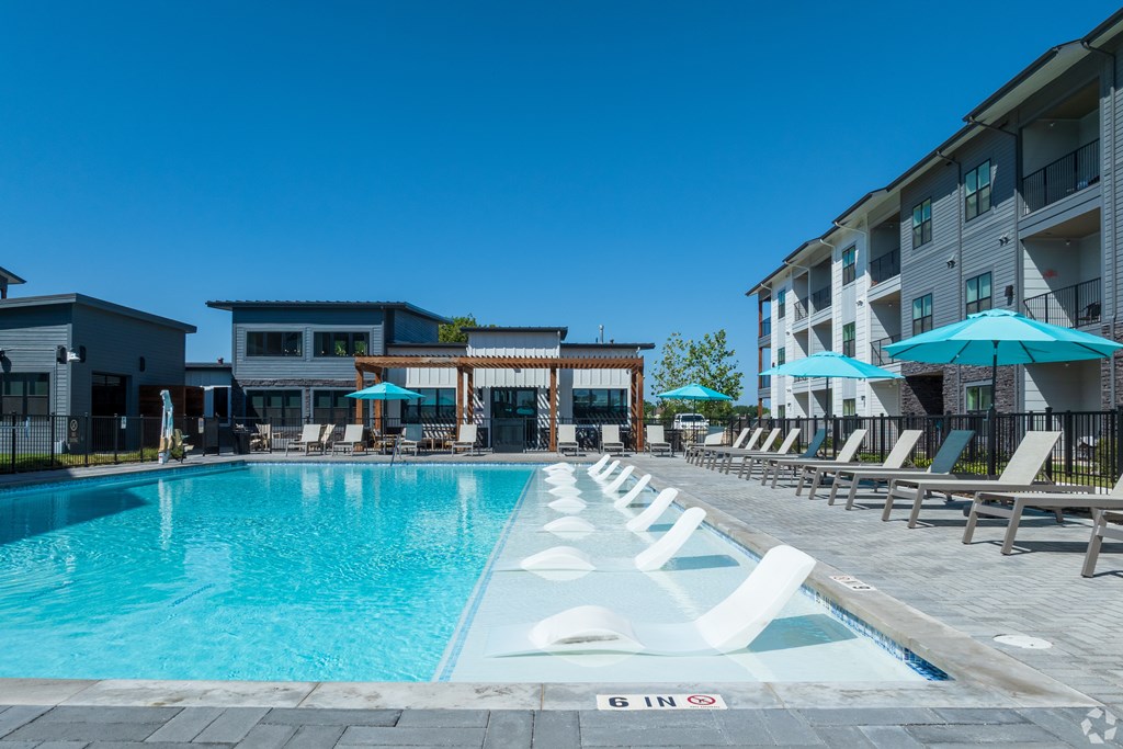 A swimming pool with lounge chairs and umbrellas in front of a building.