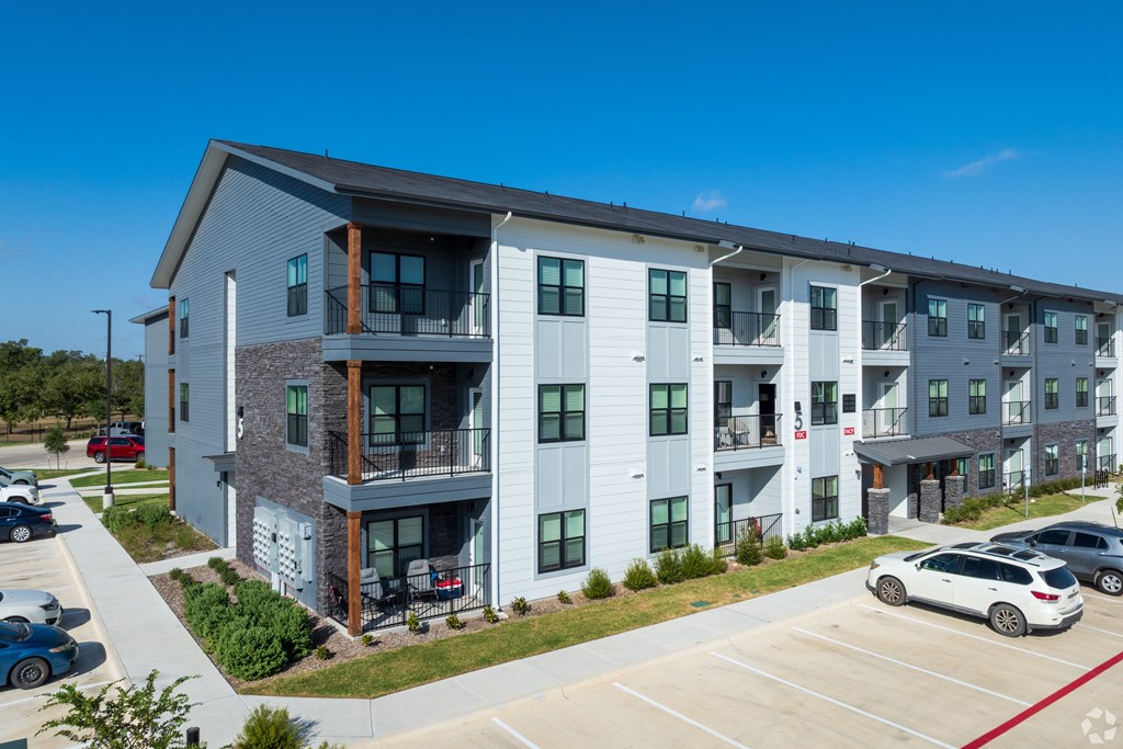 A modern apartment complex with a parking lot in front.