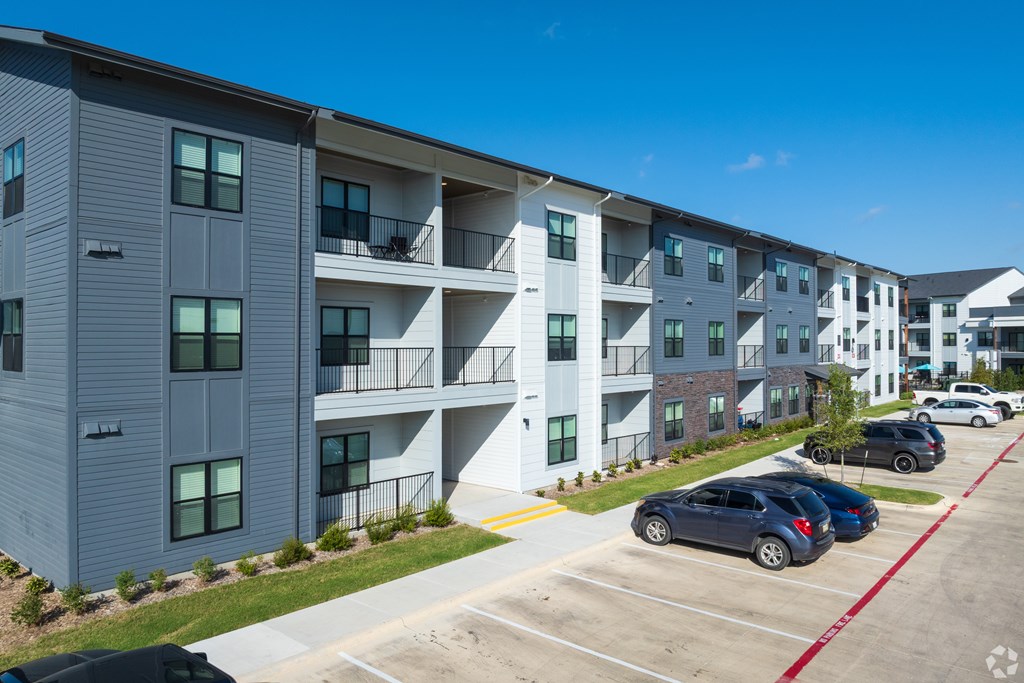 A parking lot in front of a building with cars parked.