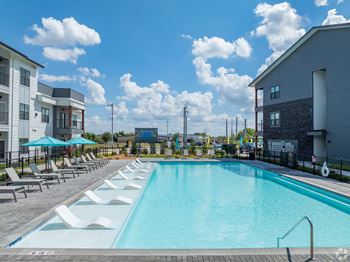 A large swimming pool with lounge chairs and umbrellas in front of a building.