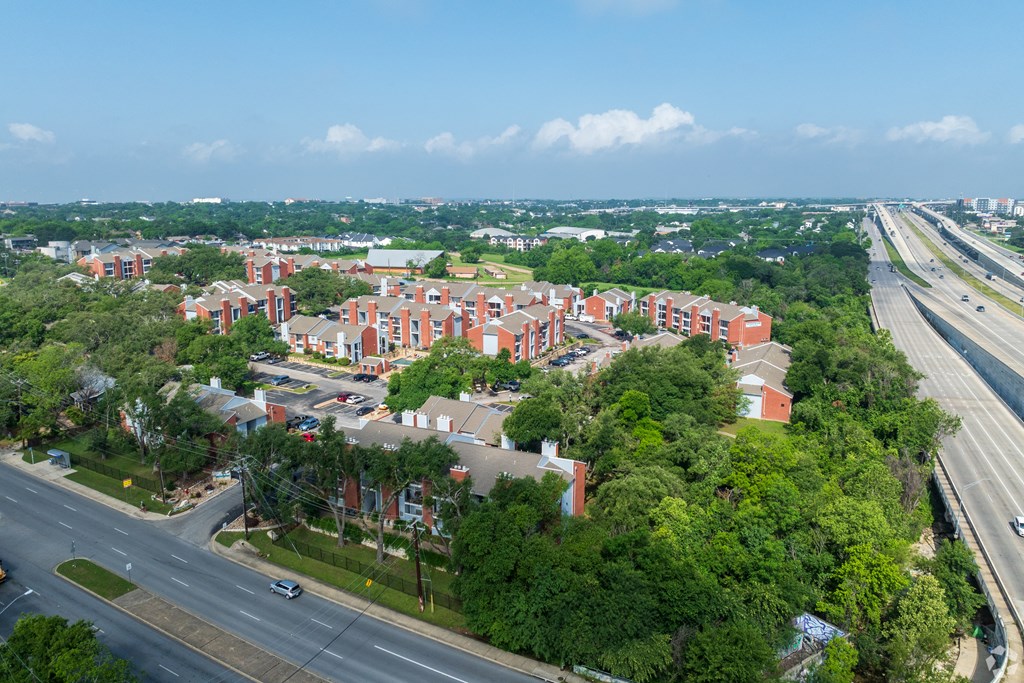 A large red brick building is surrounded by trees and is located next to a highway.