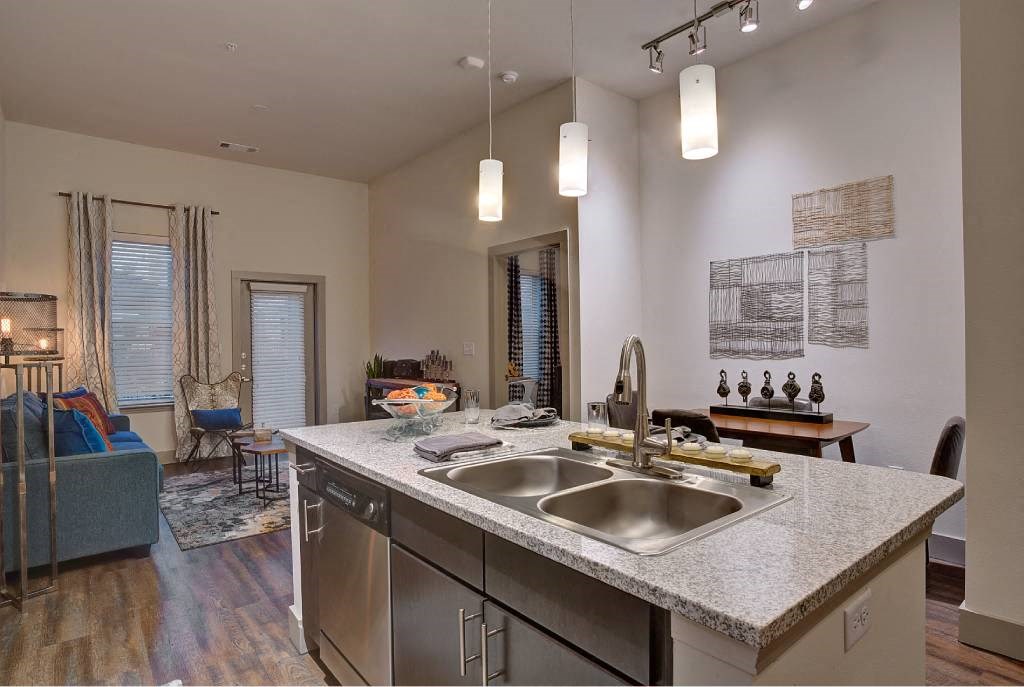 a kitchen with a sink and a view of a living room a kitchen with a sink and a view of a living room at The Grand at Stonecreek, San Marcos, TX