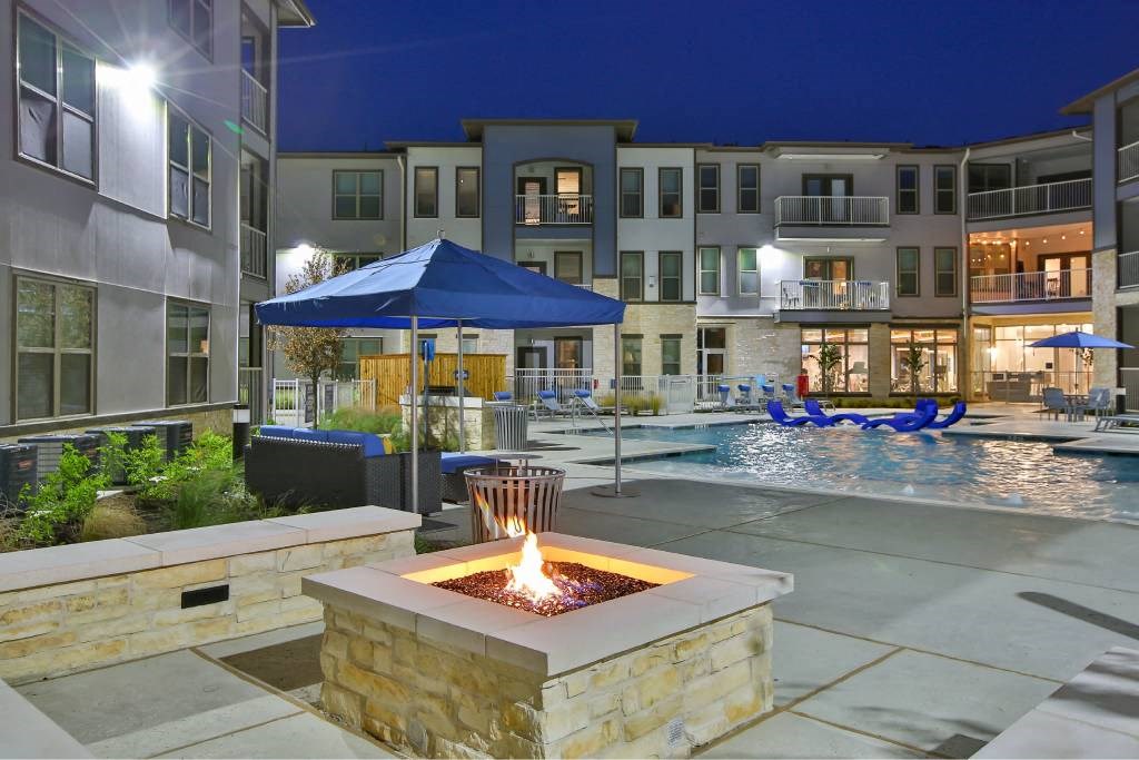 an outdoor area with a fire pit and a pool at night at The Grand at Stonecreek, San Marcos, TX, 78666