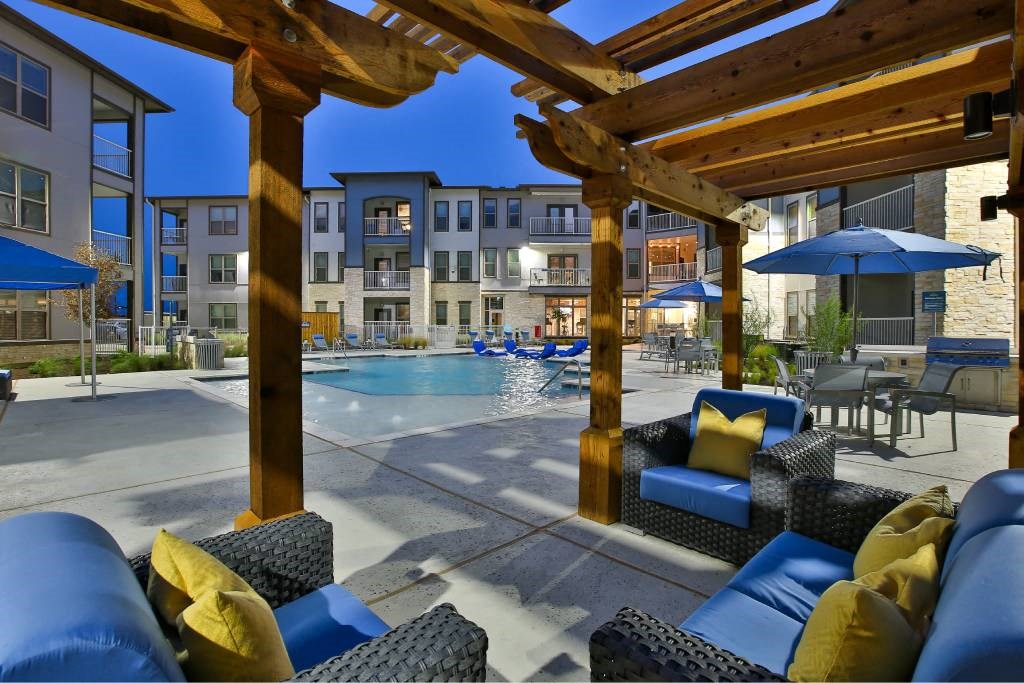 a swimming pool with chairs and umbrellas in front of a building at The Grand at Stonecreek, San Marcos, Texas
