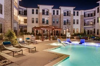 a swimming pool with lounge chairs in front of an apartment building at The Grand at Stonecreek, San Marcos, 78666