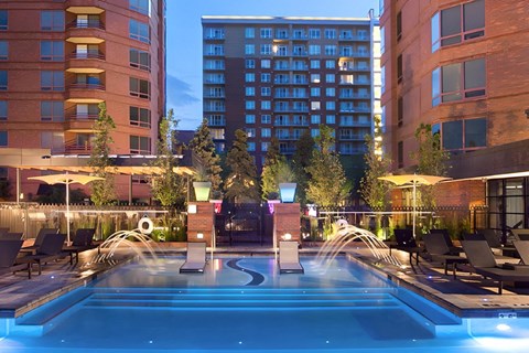 A large outdoor swimming pool surrounded by lounge chairs and lit by lights.