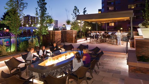 A group of people are sitting around a fire pit on a rooftop patio.