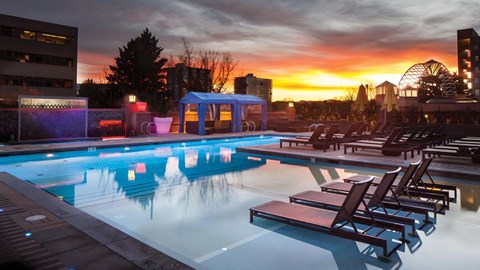 A pool with lounge chairs and a sunset in the background.