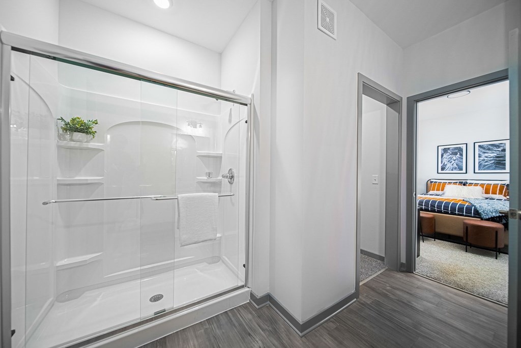 A modern bathroom with a walk-in shower and a view of a bedroom through the open door.