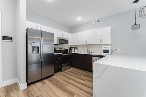 A modern kitchen with a stainless steel refrigerator and wooden flooring.